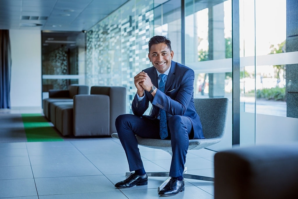 Full length portrait of happy businessman sitting with hands clasped in office lobby